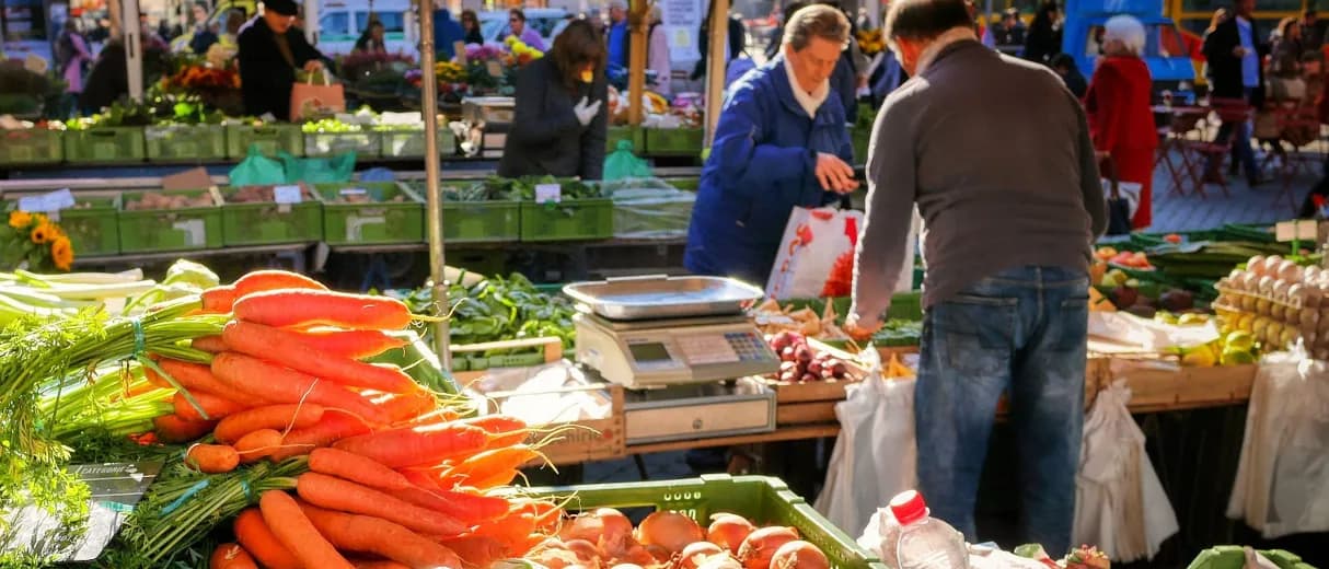 Reich bestückter Marktstand mit Zucchini, Tomaten, Paprika und Kräutern.